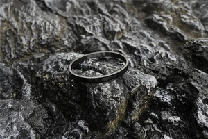 Detail of matte black titanium steel oval bangle set on a dark volcanic rock surface
