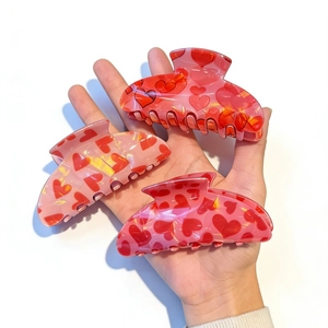 Close-up of three pink and red heart pattern hair claw clips held in hand on white background