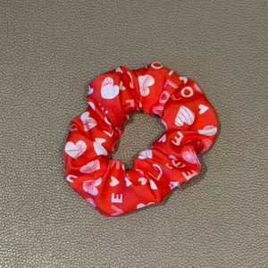 Close-up of red satin scrunchie with white heart prints and LOVE text on grey background