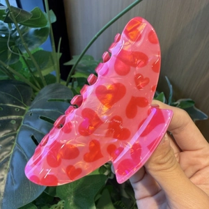 Detailed view of pink heart pattern hair claw clip with glossy finish in hand