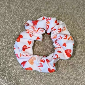 Detail of white satin scrunchie with red heart prints and LOVE text on grey surface