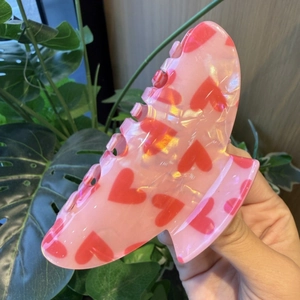 Detail of pink hair claw clip with red heart patterns shown in a close-up outdoor view