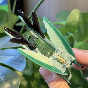 Close-up of translucent green and black swallow claw clip with golden metal spring
