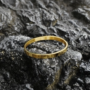 Polished gold stainless steel oval bangle on natural rock background in a minimalist style