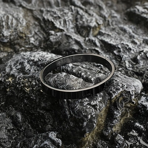 Minimalist black matte titanium steel oval bangle with mechanical hinge on volcanic rock