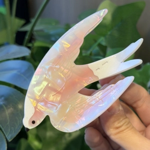 Creative swallow-shaped hair claw clip with pearlescent finish held against green leaves