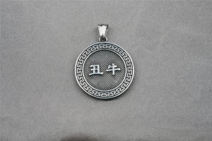 Detailed close-up of a silver zodiac pendant with ox relief and traditional patterns