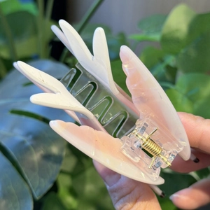 Detail of pink gradient butterfly wing hair claw clip held against green foliage