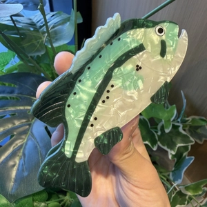 Detailed view of fish-shaped hair claw clip with green pearlescent finish held in hand