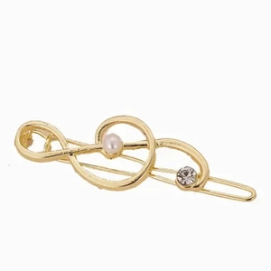 Fermaglio per capelli a nota musicale dorata con perla e strass su sfondo bianco