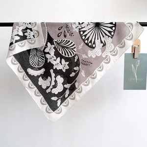 Detail of a square silk scarf with floral patterns and scalloped edges hanging on a rod
