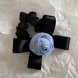 Détail d'un chouchou en satin noir orné d'une rose en soie bleue sur papier blanc