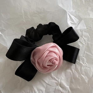 Détail d'un chouchou en satin noir orné d'une rose en soie rose et d'un nœud