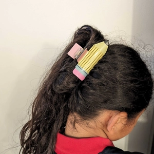 Détail d'une pince à cheveux créative en forme de crayon jaune et rose sur une queue de cheval