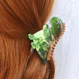 Detail view of a green acetate dinosaur hair claw clip styled on long brown hair