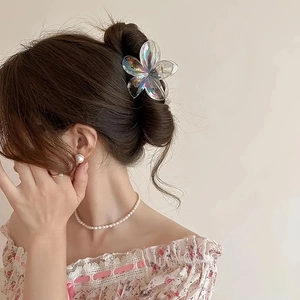 Vue détaillée d'une pince à cheveux fleur de frangipanier irisée sur un chignon élégant