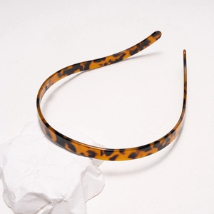 Detail shot of thin tortoiseshell acetate headband on a white textured stone base