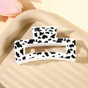 Rectangle cow print hair claw clip in black and white on a textured aesthetic tray