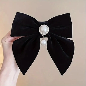 Detail of a large black velvet bow hair clip featuring a pearl pendant and small rhinestones