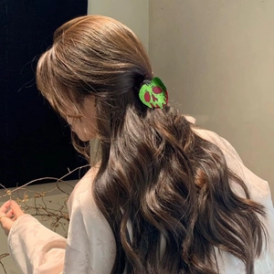 Close-up of green and red skull apple hair claw clip styled on dark wavy hair