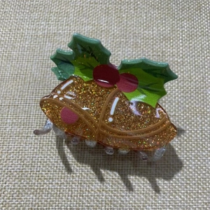 Christmas hair claw clip featuring golden glitter bells and green holly leaves on burlap