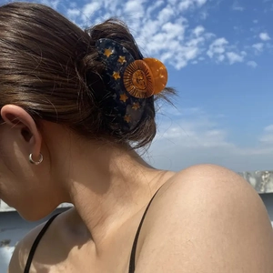Fashionable acetate hair claw with yellow stars and sun on brown hair against blue sky