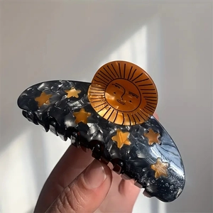 Acetate sunflower hair claw clip with star patterns and a sun face on a dark marble base