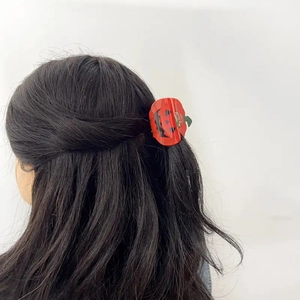 Detail of red Jack-o'-lantern pumpkin hair claw clip styled on dark long hair