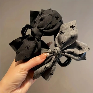 Detail showing high-quality black and grey fabric bow claw clips held in hand for hair styling