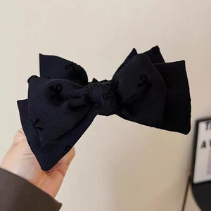 Detailed close-up of a large black layered bow hair claw made of textured twill fabric