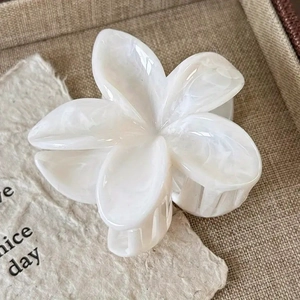 Elegant marble white plumeria hair claw clip on a textured tray with creative props