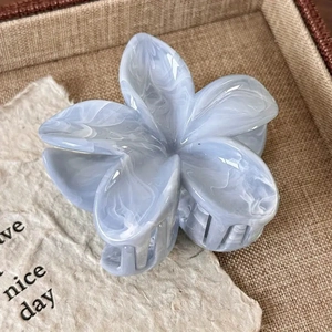 Macro detail of blue marble textured floral hair claw clip on a rustic linen tray