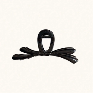 Pince à cheveux noire brillante en forme de nœud avec un design élégant sur fond beige
