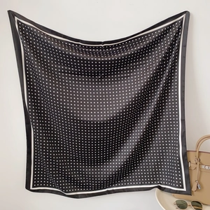 Dettaglio di un foulard in seta a pois accanto a una borsa e occhiali da sole