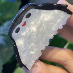 Pinza para el pelo con forma de pingüino y acabado perlado sostenida frente a plantas