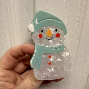 Détail de la pince à cheveux bonhomme de neige avec finition nacrée et écharpe bleue