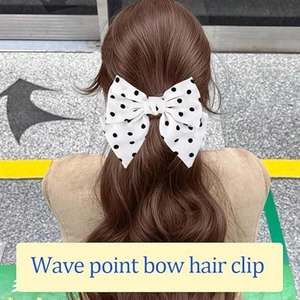 Close-up of white polka dot bow hair clip worn on long wavy brown hair for styling