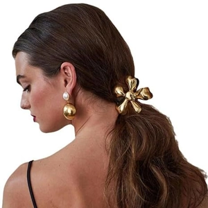 Detail of elegant gold metal flower hair claw and pearl ball drop earrings on model