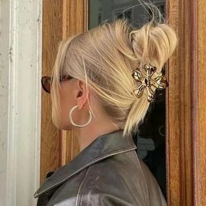 Detailed side view of a large golden metal flower hair claw clip worn by a model