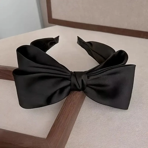Elegante cerchietto in raso nero con doppio fiocco e design antiscivolo su fondo legno