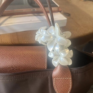 Détail d'une élégante pince à cheveux en forme de fleur blanc nacré sur un sac à main