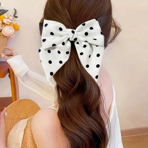 Sweet white polka dot bow hair clip on model's dark brown wavy hair for a summer look