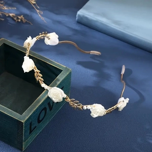 Detail of white fabric roses, gold leaves, and pearls on a vintage metal headband