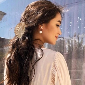 Close-up of golden shell hair clip and pearl earrings worn by a model in detail