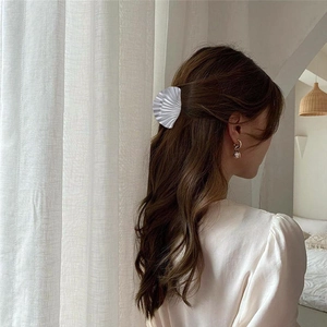 Detail of silver shell hair claw clip with pearl earrings on a model in soft lighting