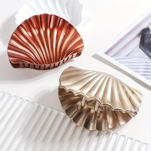 Elegant shell-shaped hair claw clips in metallic gold and bronze finishes on a tray