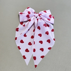 Détail du nœud papillon rose clair avec motifs de cœurs rouges et longs rubans pendants