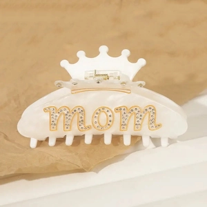 Dettaglio molletta a corona bianca con scritta MOM in strass su carta beige