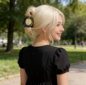 Detail of a large black hair claw clip with celestial sun face pattern on blonde hair