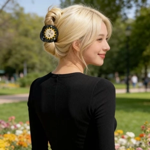 Black circular hair claw with sun print shown on a blonde model in a park